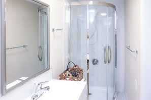 Une salle de bain moderne avec une douche à parois de verre, un lavabo blanc et un grand miroir.