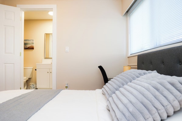 A bedroom with a bed, a bedside table, a window with blinds, and a door leading to a bathroom.