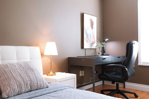 A bedroom with a bed, bedside table, lamp, desk, chair, and a framed picture on the wall.