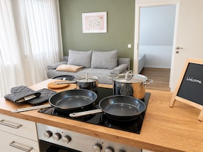 Eine Küche mit Herd, Töpfen, Pfannen und einer Tafel mit dem Schriftzug 'Welcome'.
