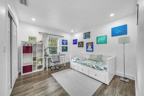 A bedroom with a bed, desk, chair, and a collection of artwork on the walls. - Miami Home: Private Yard, Near Beaches & Dining (Miami)
