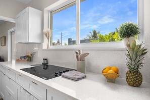 A modern kitchen with a built-in stove, white cabinets, a window with a view of greenery, and a small plant on the windowsill.