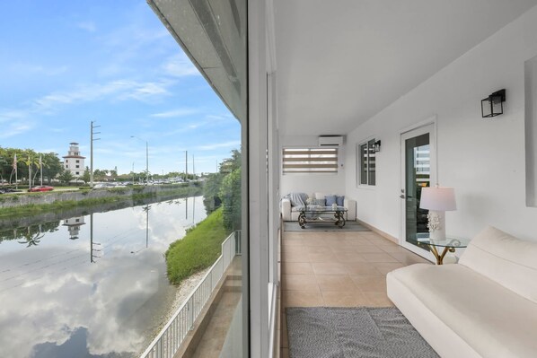 A modern living room with a view of a canal, a white sofa, a glass coffee table, and a lamp.