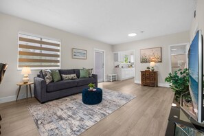 A living room with a sofa, a coffee table, and a rug. There is a kitchen in the background with cabinets and a countertop. - Canal-View Terrace, Family-Friendly, 5 Min to MIA (Miami Springs)