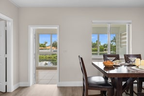 A dining area with a table set for two, a view of a garden through a window, and a door leading outside.