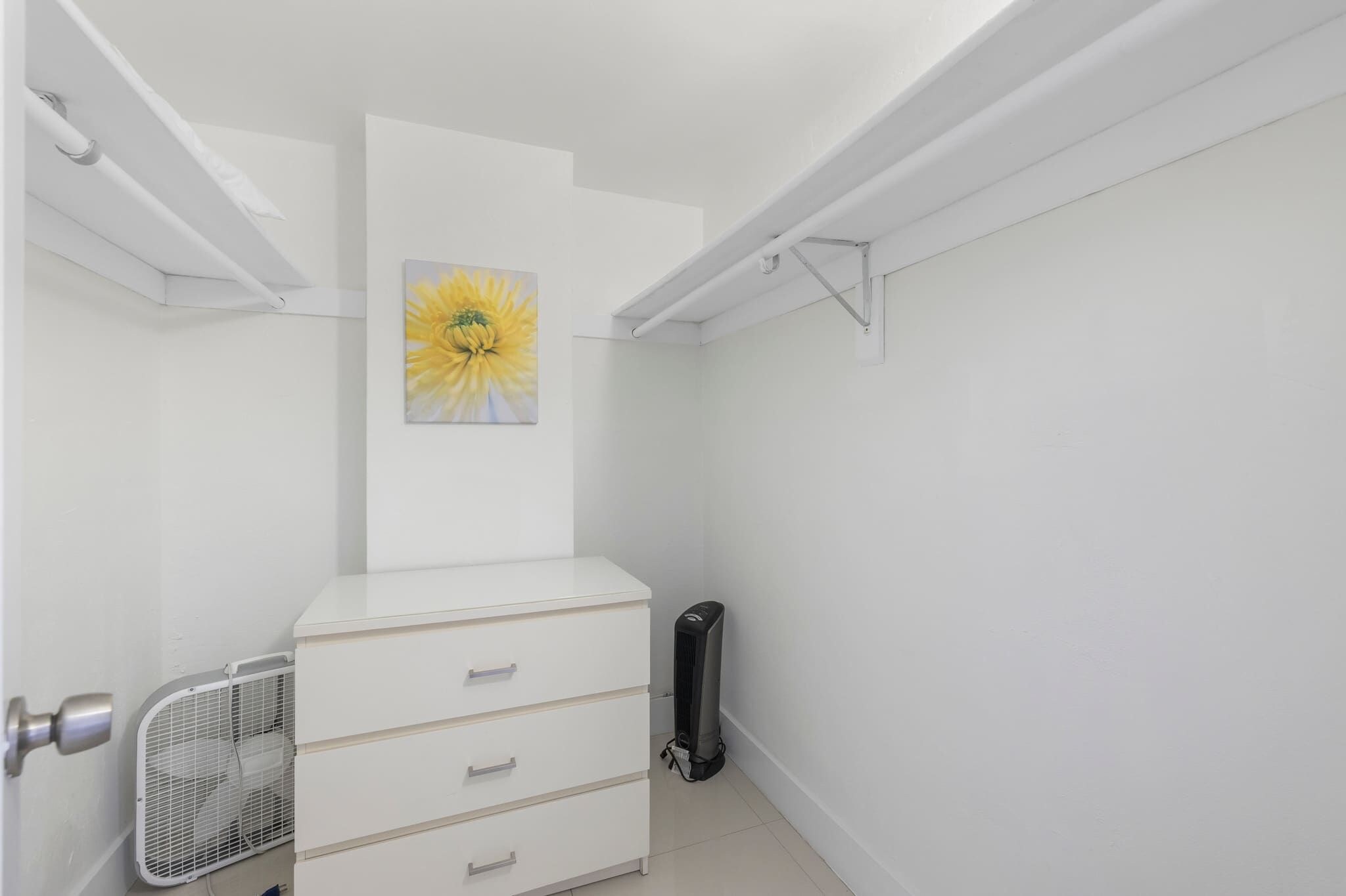 Un placard blanc avec une commode blanche, un radiateur et un tableau représentant une fleur, accroché au mur.