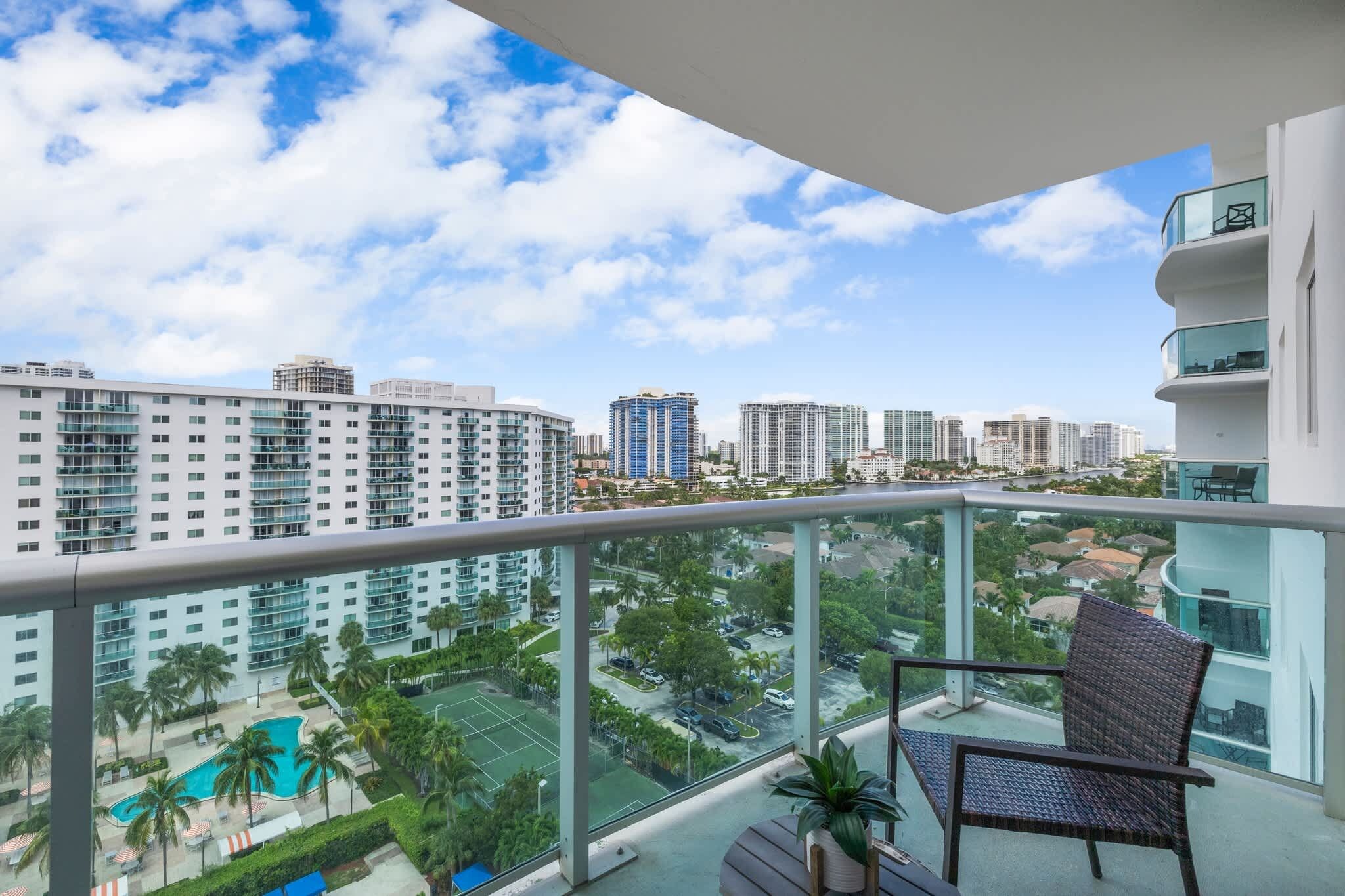 A balcony with a view of a cityscape, including high-rise buildings and a tennis court.