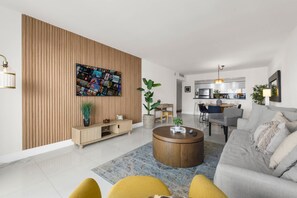 A modern living room with a wooden accent wall, a round coffee table, and a grey sofa. - Beachside Apartment w/ Heated Pool & Free Parking (Sunny Isles Beach)