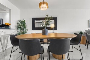 A modern dining area with a round wooden table, black chairs, a central vase with greenery, and a hanging light fixture. - Beachside Apartment w/ Heated Pool & Free Parking (Sunny Isles Beach)