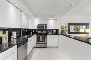 Eine moderne Küche mit weißen Schränken, schwarzen Arbeitsplatten, Edelstahlgeräten und einem eingebauten Ofen.