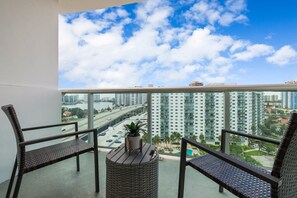 A balcony with two wicker chairs, a small table, and a potted plant. - Beachside Apartment w/ Heated Pool & Free Parking (Sunny Isles Beach)