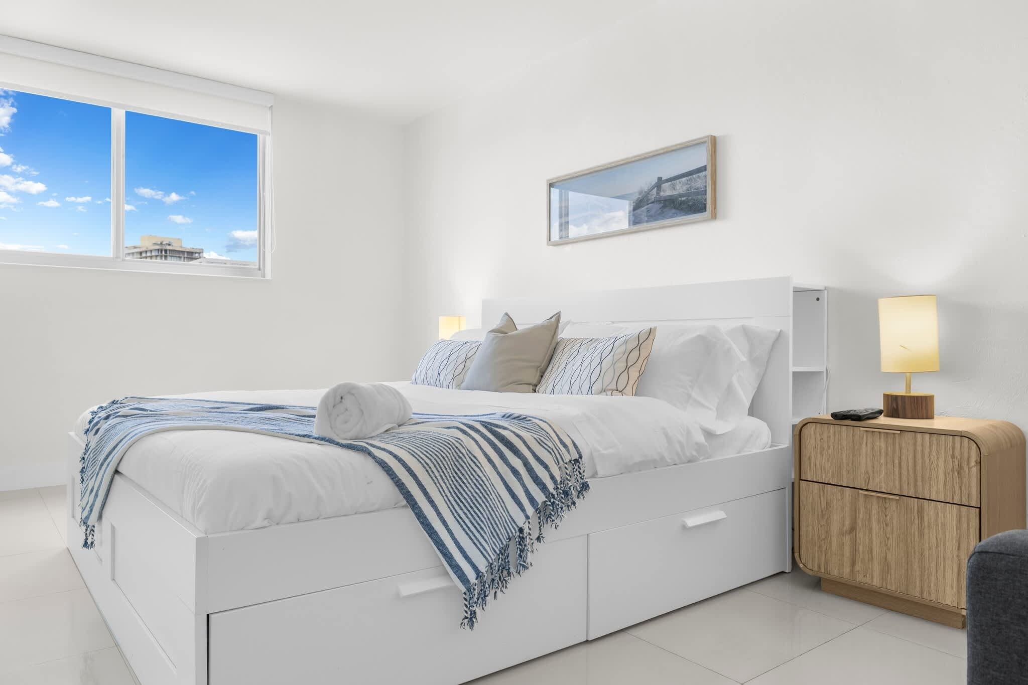 A modern bedroom with a bed, bedside tables, a nightstand, a lamp, and a framed picture on the wall.