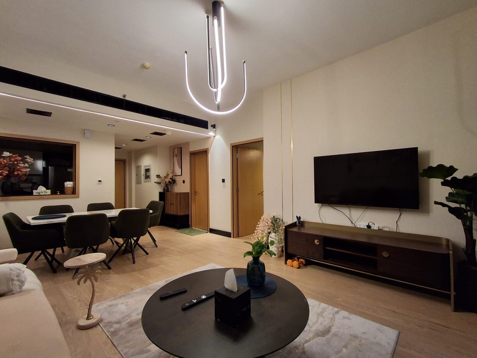 Una sala moderna con televisor de pantalla plana, una mesa de centro redonda y un comedor con sillas y una mesa.
