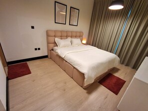 Une chambre à coucher moderne avec un grand lit, une lampe de chevet et une vue sur l’extérieur à travers les rideaux.
