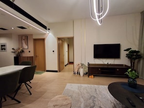 A modern living room with a flat-screen TV, a dining area with chairs, a marble coffee table, and a plant. - POMMA HOLIDAYS Spacious 1BR Retreat in Dubai JVC Sleeps 4 with Modern Amenities (Dubai)