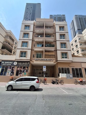 Un immeuble résidentiel à plusieurs étages, doté de balcons, avec une voiture garée devant et une enseigne indiquant « AL QASAS GENT'S SALON » au rez-de-chaussée.
