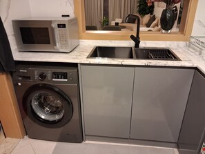 A compact kitchen with a washing machine, a microwave, and a sink. - POMMA HOLIDAYS Spacious 1BR Retreat in Dubai JVC Sleeps 4 with Modern Amenities (Dubai)