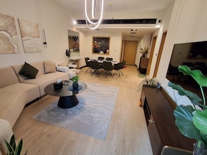 A modern living room with a sofa, coffee table, dining area, and a TV. - POMMA HOLIDAYS Spacious 1BR Retreat in Dubai JVC Sleeps 4 with Modern Amenities (Dubai)