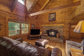 L’intérieur d’un chalet en bois est doté d’une cheminée en pierre, de canapés en cuir et d’un téléviseur posé sur un meuble en bois.