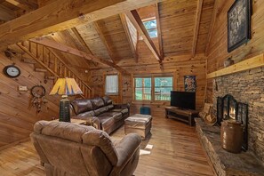 A log cabin interior with a wooden ceiling, a fireplace, a sofa, a television, and a window with a view. - Hummingbird Hideaway, Log Cabin w/Cozy Mountain Vibes, Dog Friendly-Fenced Yard (Franklin)