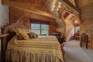 A log cabin bedroom with a large bed, a chair, a desk, and a window. - Hummingbird Hideaway, Log Cabin w/Cozy Mountain Vibes, Dog Friendly-Fenced Yard (Franklin)