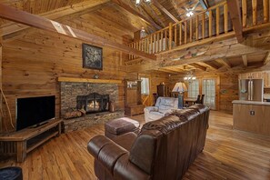 L’intérieur d’une cabane en rondins, avec une cheminée en pierre, un canapé en cuir, un plancher en bois et un coin cuisine.