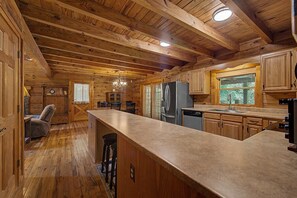 A wooden cabin interior with a kitchen area, wooden ceiling beams, and a bar counter. - Hummingbird Hideaway, Log Cabin w/Cozy Mountain Vibes, Dog Friendly-Fenced Yard (Franklin)