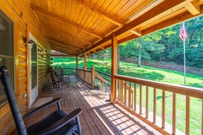 A wooden cabin with a covered porch, outdoor seating, and a view of a green landscape. - Hummingbird Hideaway, Log Cabin w/Cozy Mountain Vibes, Dog Friendly-Fenced Yard (Franklin)