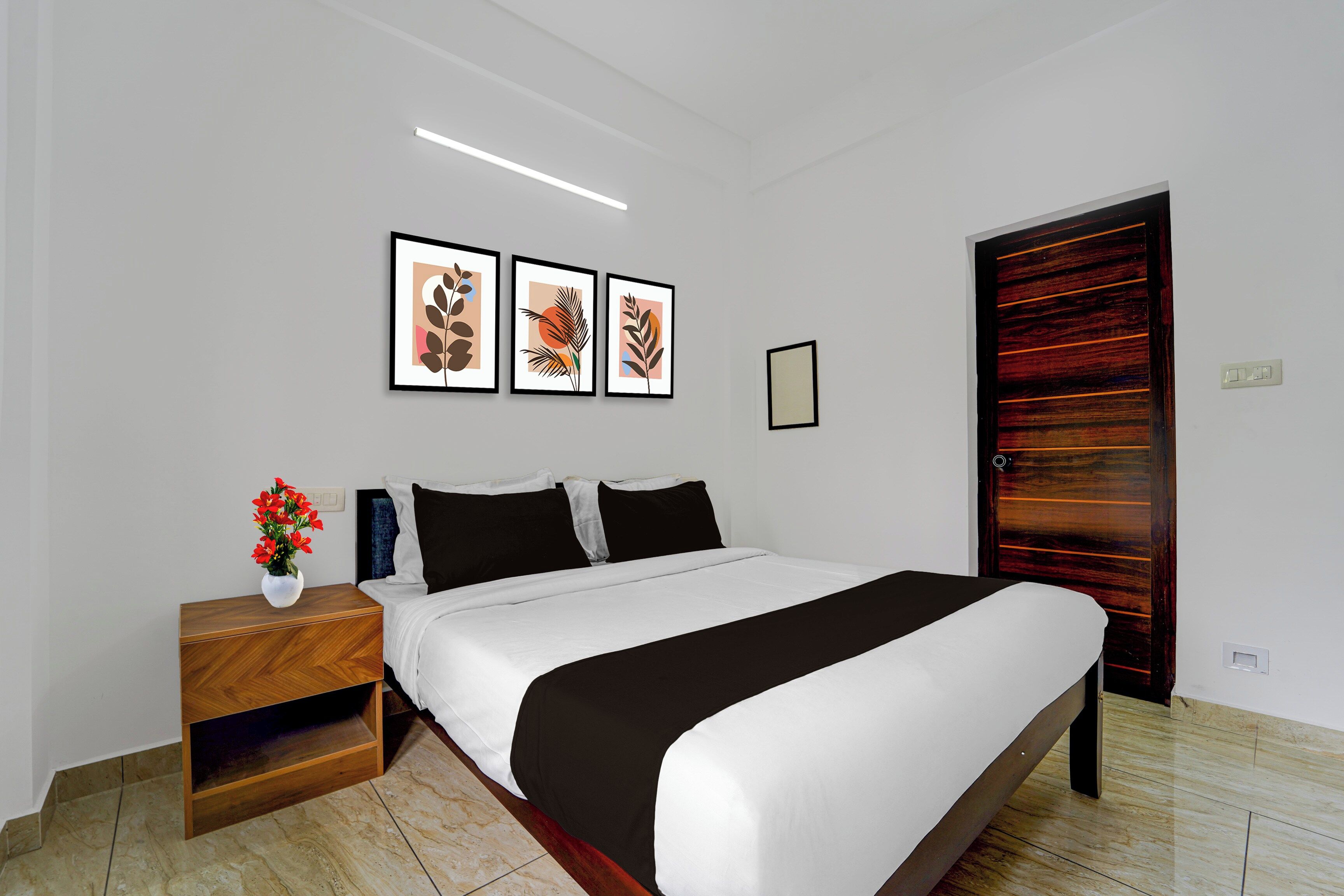 A bedroom with a bed, bedside table, and a nightstand with a vase of flowers. There are three framed pictures on the wall above the bed.