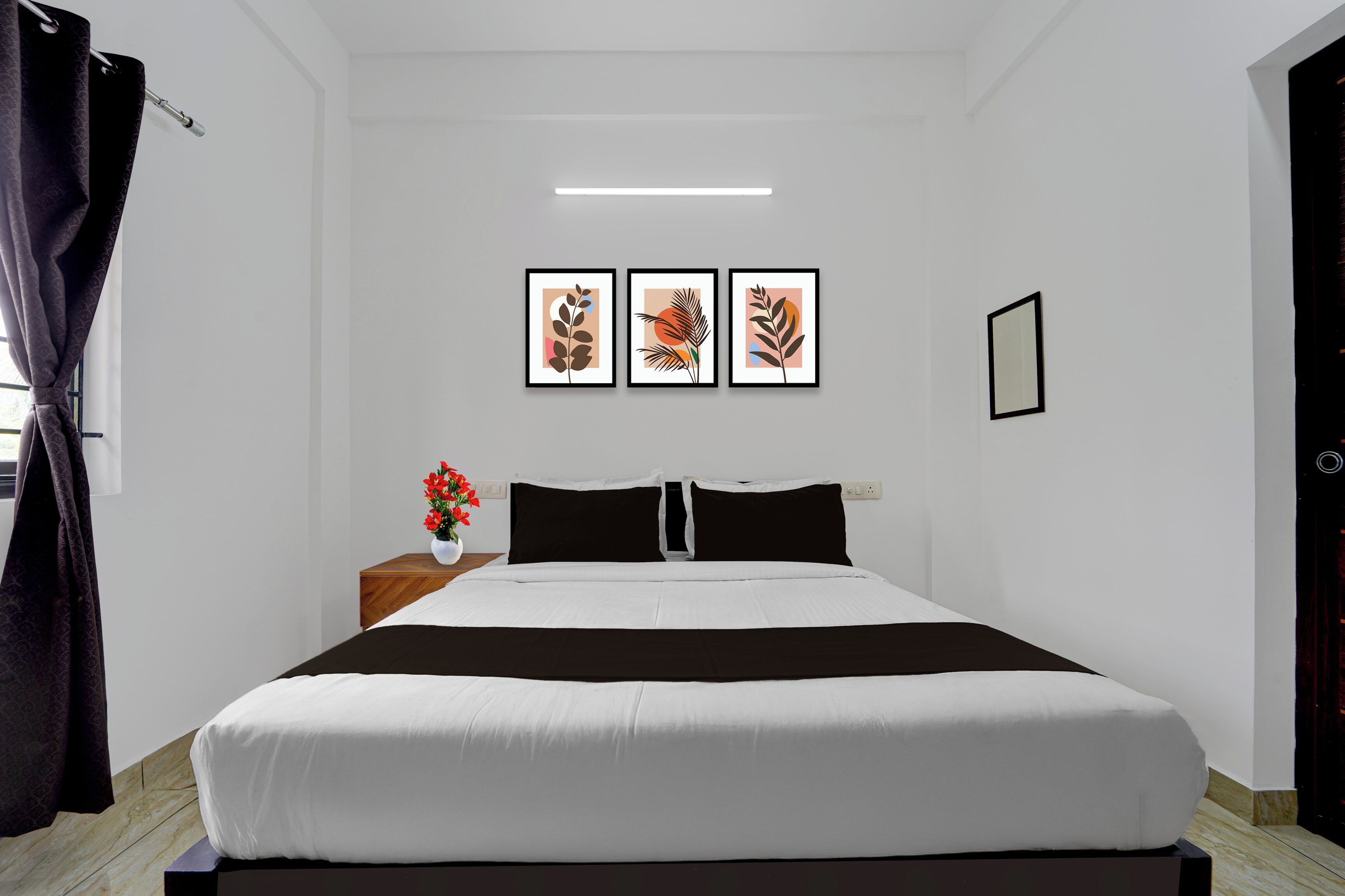 A bedroom with a bed, a nightstand with a vase of flowers, and three framed artworks on the wall.