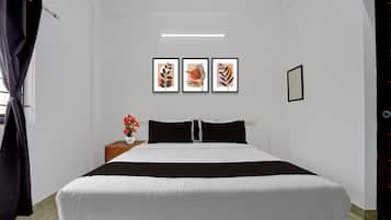 A bedroom with a bed, a nightstand with a vase of flowers, and three framed artworks on the wall.