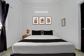 A bedroom with a bed, a nightstand with a vase of flowers, and three framed artworks on the wall.