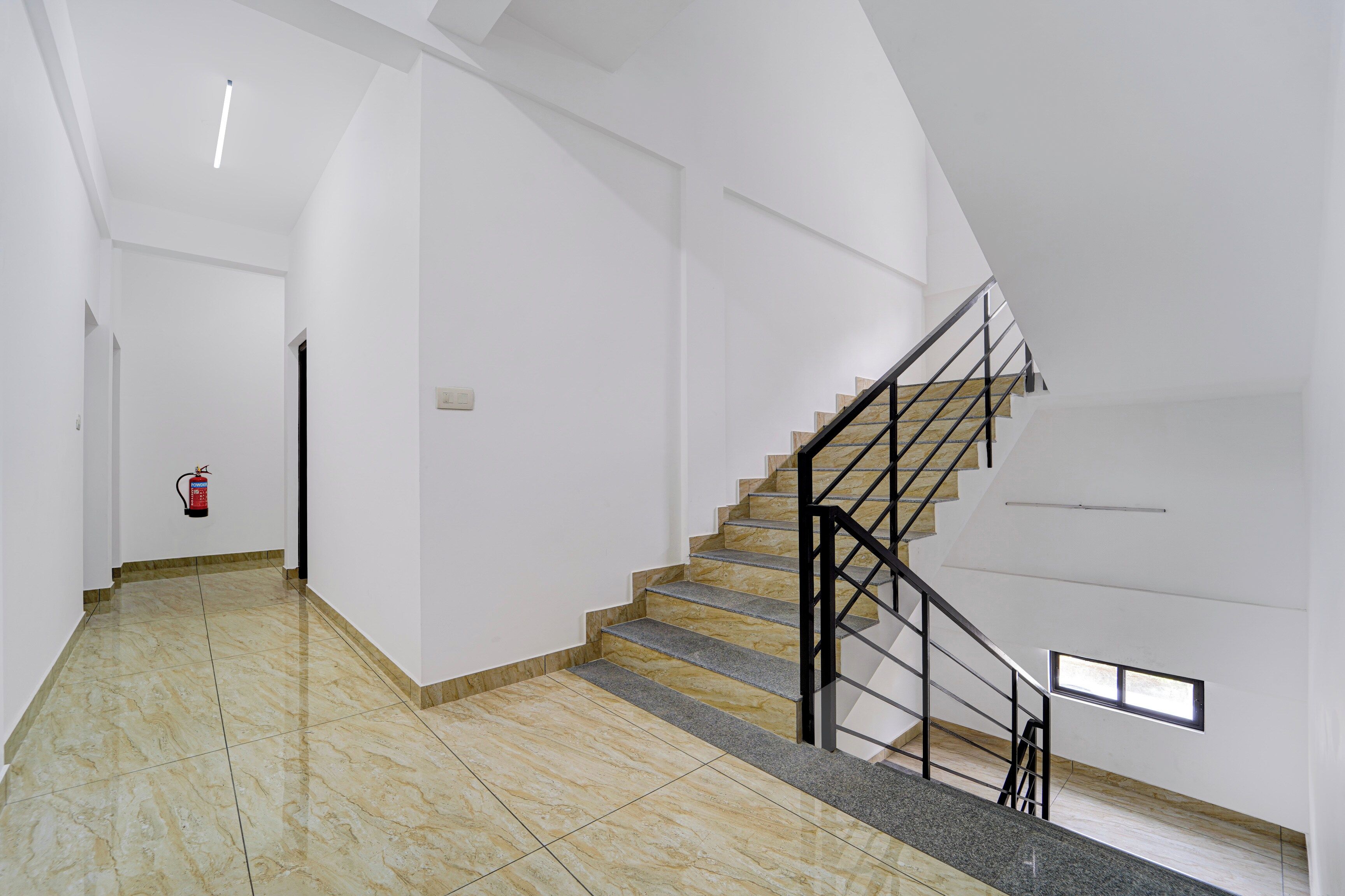 A spacious interior with a marble floor, a staircase with a metal railing, and a fire extinguisher mounted on the wall.
