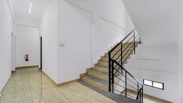 A spacious interior with a marble floor, a staircase with a metal railing, and a fire extinguisher mounted on the wall.
