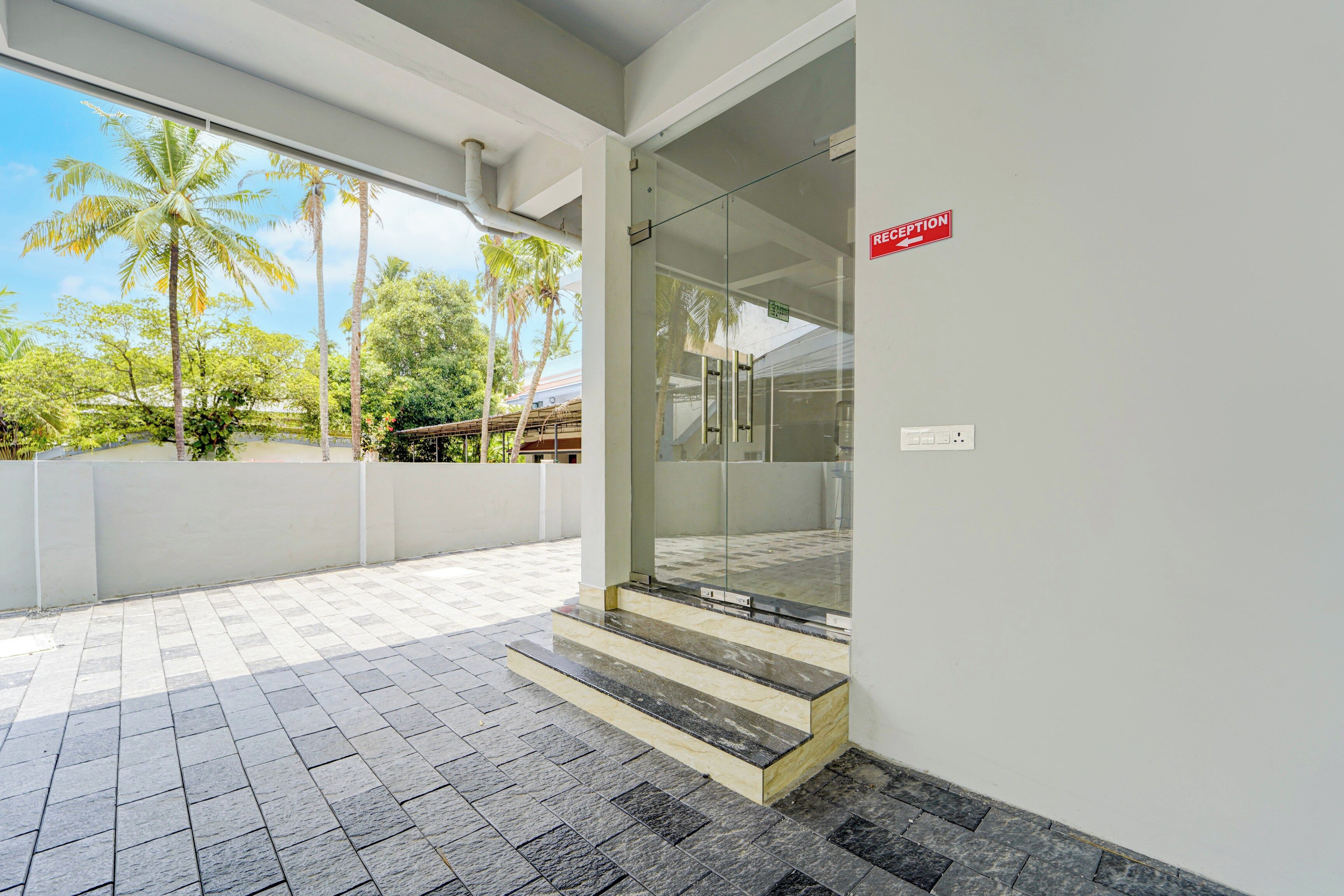 A reception area with a glass door, a reception sign, and a view of palm trees outside.