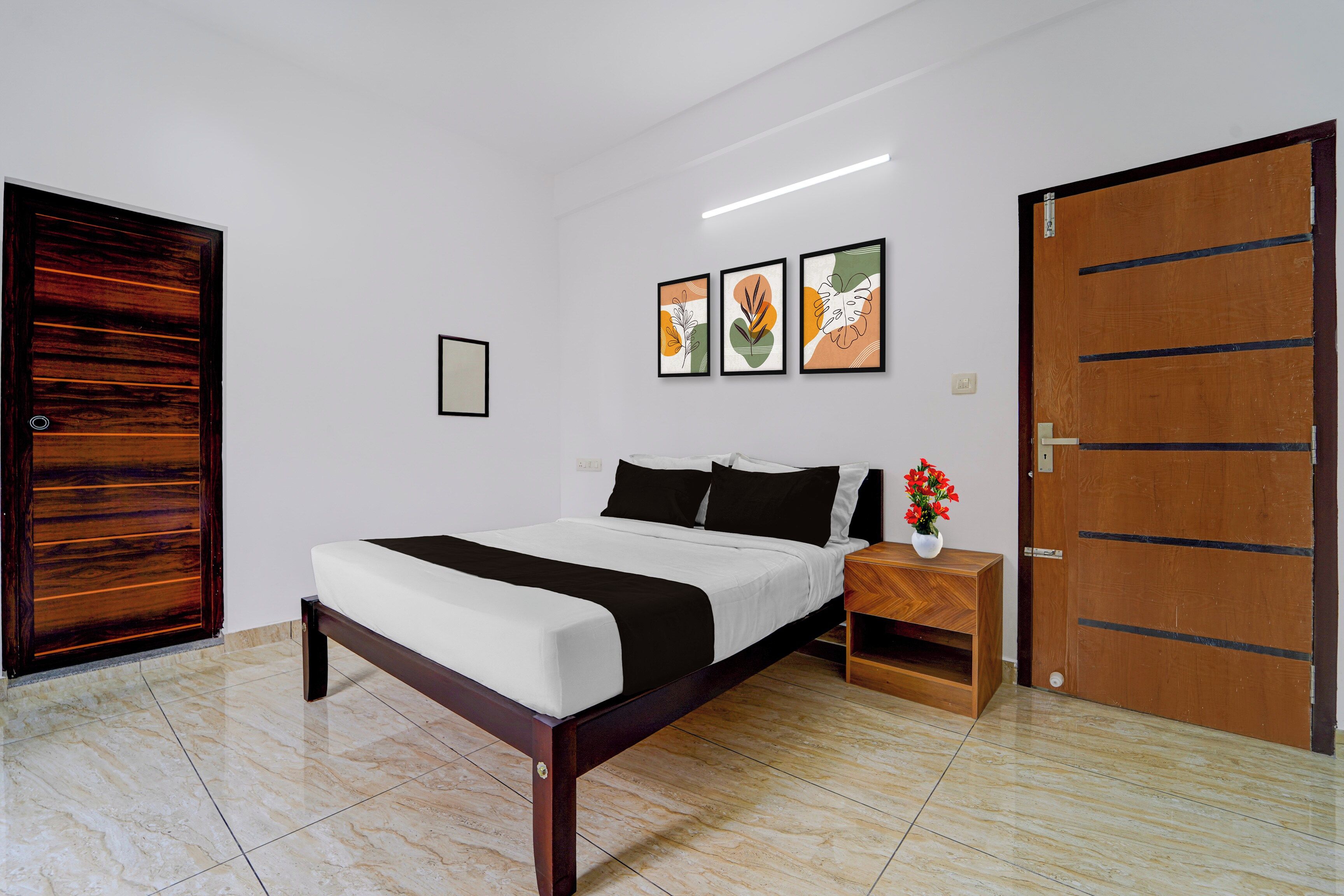 A bedroom with a bed, a nightstand, a wooden wardrobe, and three framed artworks on the wall.