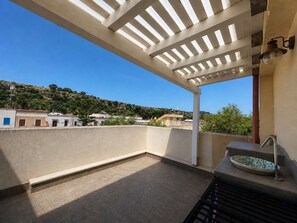 Terraço no telhado com pérgola, pia e vista para um morro com edifícios.