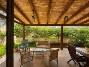 An outdoor patio with wicker furniture, a brick wall, and a view of greenery. - The Secret Garden, villa with private garden (San Vito Lo Capo)