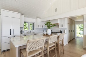 A modern kitchen with white cabinetry, a large island with bar stools, and a view of the outdoors through a window. - Island on Lake Joe! Cozy and rustic 5Bed 3Bath with 399' of shoreline! (MacTier)