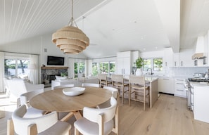 Une cuisine spacieuse avec des meubles blancs, un coin repas doté d’une table ronde en bois et une grande fenêtre offrant une vue sur l’extérieur.