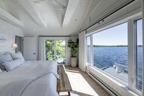 Une chambre avec un grand lit, un banc, une plante en pot et une vue sur l’eau.