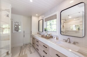 Une salle de bain moderne avec des meubles blancs, un grand miroir et un espace douche.