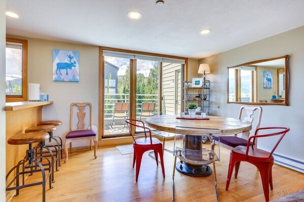 A dining area with a round table and chairs, a bar with stools, a large window, and a sliding glass door leading to an outdoor patio. - Winter Park Condo w Hot Tubs, Views & Loft! (Winter Park)