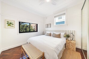 Une chambre à coucher avec un lit, une fenêtre, une table de chevet avec une lampe et un banc.