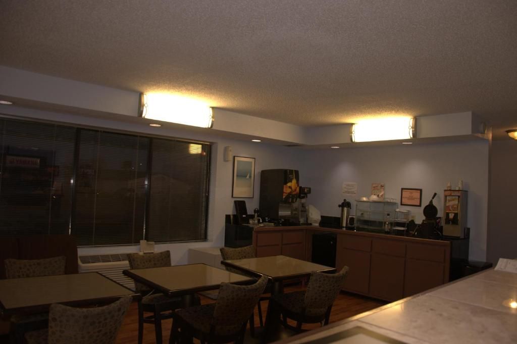 A dining area with a table and chairs, a kitchen area with appliances, and a large window with blinds.