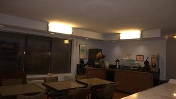 A dining area with a table and chairs, a kitchen area with appliances, and a large window with blinds.