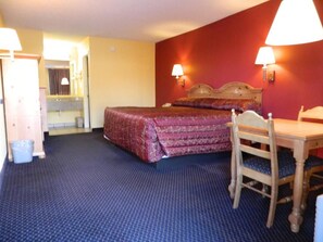 A hotel room with a bed, a desk, and a chair. There is a lamp on the wall and a trash bin. - Bestway Inn (Rock Hill)