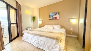 A hotel room with a bed, a painting on the wall, and a view through the glass door. - SA - Clube XV - Apto CXV2103 (Santos)