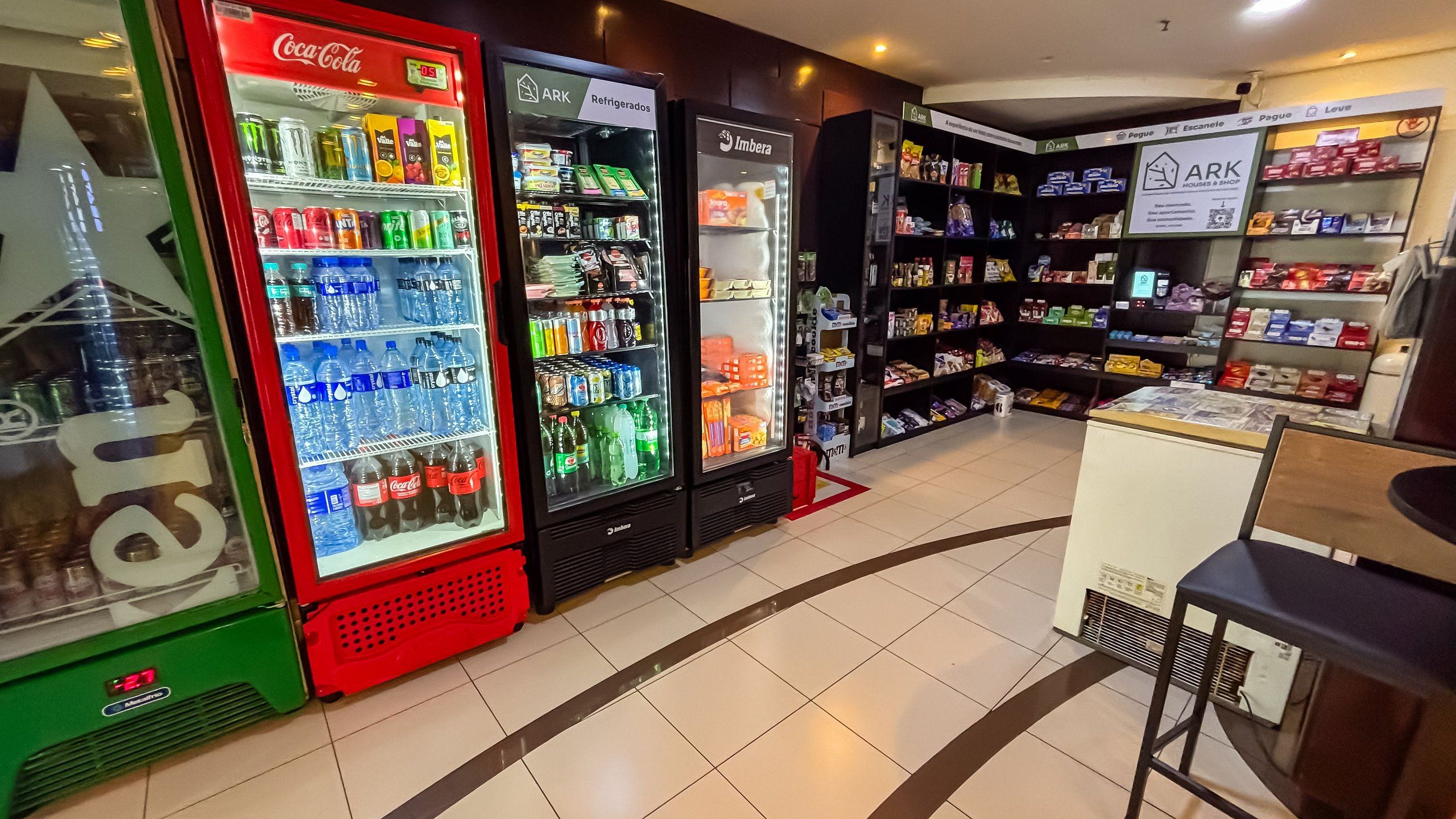 Una tienda con varias máquinas expendedoras de bebidas, incluyendo máquinas de Coca-Cola y de la marca ARK, y estantes llenos de diferentes productos.