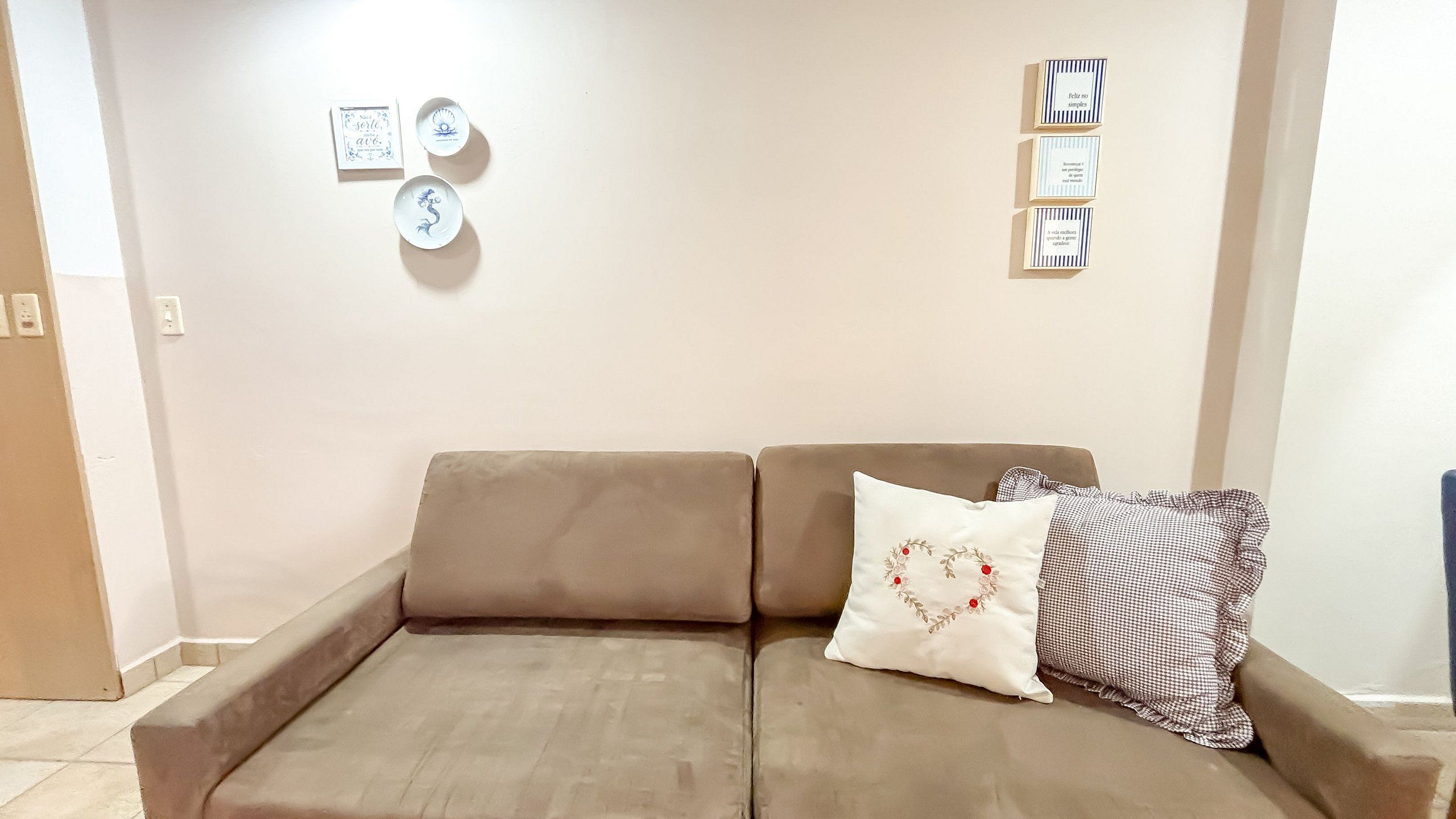 A beige sofa with two pillows, one with a heart design, and three framed items on the wall.